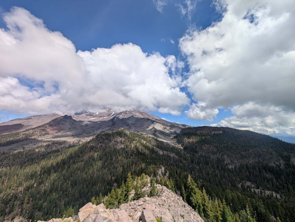 White clouds and blue skies above many conifers in Mount Shasta. Photo by R. Redlich.